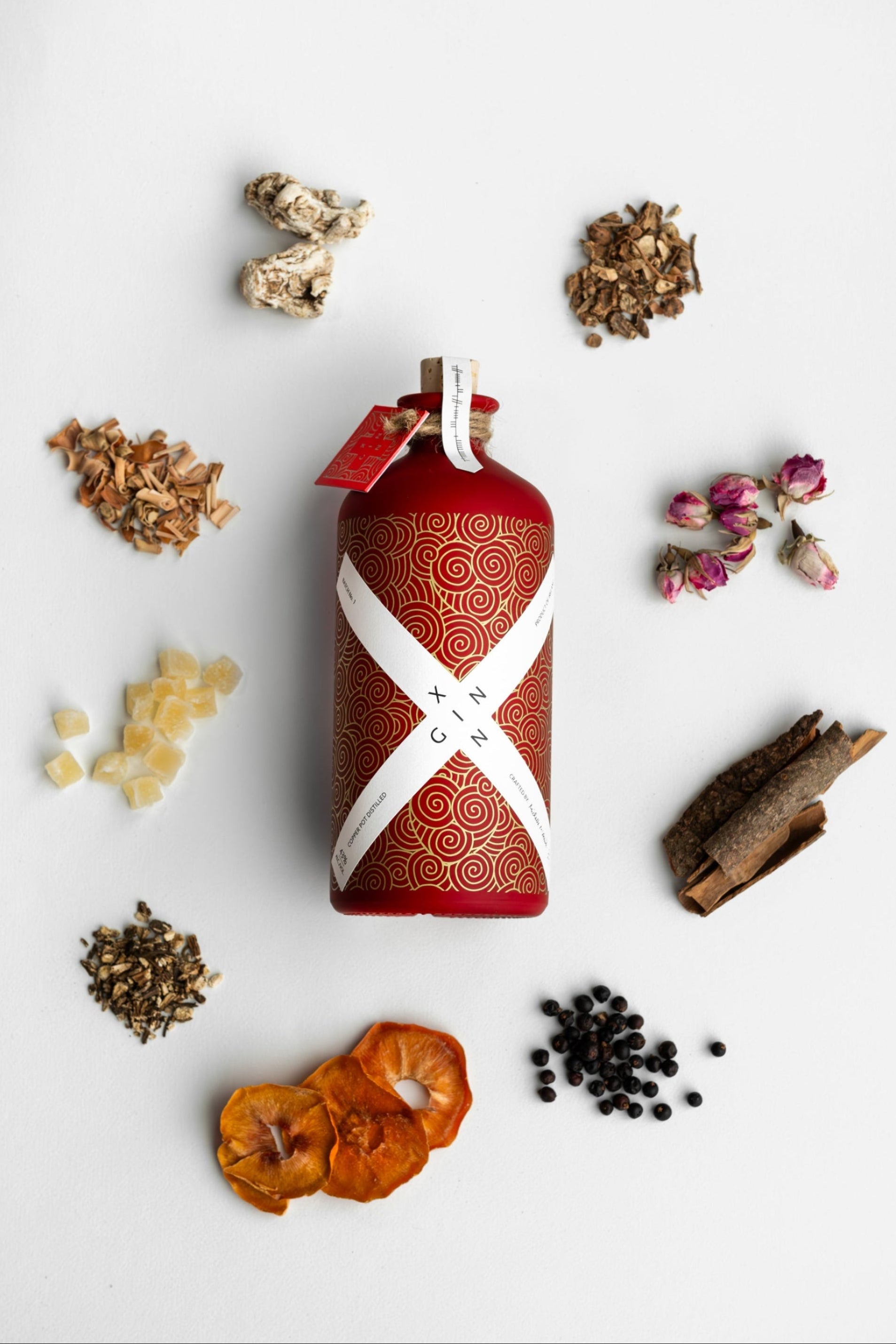 Red bottle with white pattern surrounded by dried herbs and flowers on a light background
